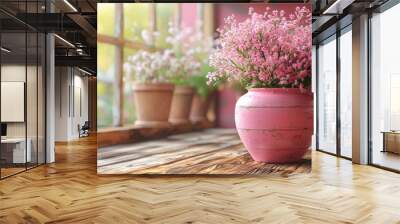 Pink pot of flowers on a wooden table near a sunlit window with additional pots in the background during the day Wall mural