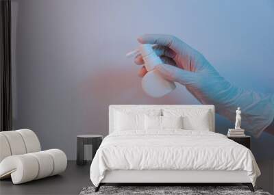 The doctor's hand in the white medical glove holding a spray, isolated in the purple background, health care concept   Wall mural