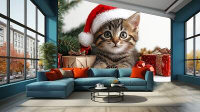 A cute kitten wearing a Santa hat, sitting beside a Christmas tree with gifts underneath Wall mural