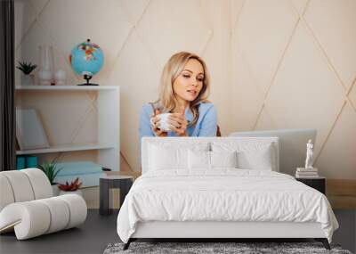 Beautiful business woman is using a laptop drinking coffee and working in office        Wall mural