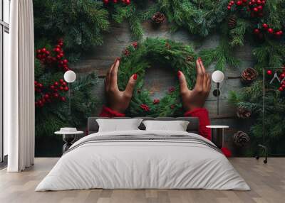 female dark skinned hands in a red sweater making christmas wreath, on wooden table background, top view Wall mural