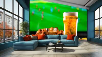 A glass of beer and hot chicken wings on a dark wooden table with crushed potato chips. Football on a background, high resolution Wall mural