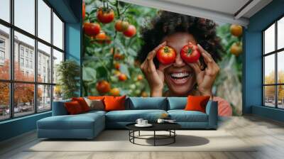 Smiling woman holding tomatoes over her eyes in a greenhouse. Wall mural