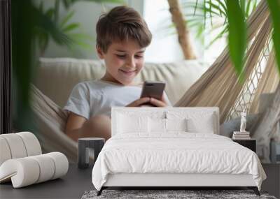 Young boy smiling while using a smartphone in a hammock. Wall mural