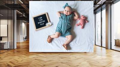 10 Ten months old baby girl laying down on white background with letter board and teddy bear. Flat lay composition. Wall mural