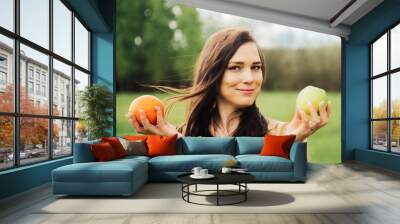 Portrait Of Young Girl. beautiful woman holding green apple and orange deciding what to choose. Wall mural