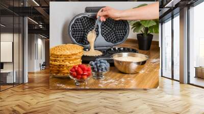 Making Belgian waffles. Female hand pours dough into waffle maker in kitchen at home. Cooking summer breakfast with round waffles and berries Wall mural