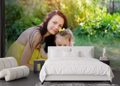 Mom and daughter in the summer park. Mom in a yellow dress and daughter with a bow on her head toy hug and laugh in the sun Wall mural