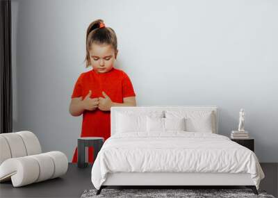 shy child girl in a red dress looks bottom. girl posing in studio     Wall mural