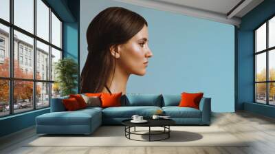 Young girl with smooth shiny skin in profile on a blue background, close-up Wall mural