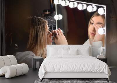 Young teenage girl attaching fake eye lashes in front of vanity mirror with lights Wall mural