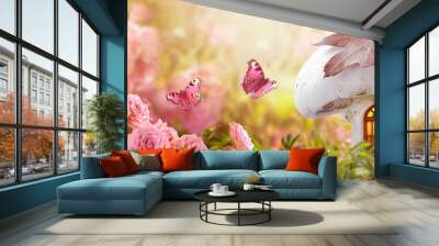 Magical fantasy elf or gnome mushroom house with window and flying butterflies in enchanted fairy tale garden, fabulous fairytale blooming pink rose flower field, shiny glowing sun light in morning Wall mural