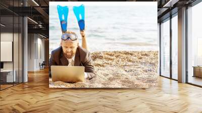 Successful businessman wearing snorkeling tools is working on the beach with laptop Wall mural