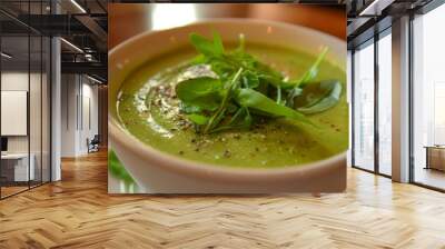 Creamy green pea soup is served in a white bowl, garnished with fresh arugula and spices Wall mural