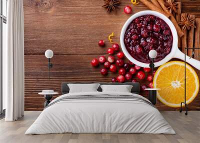 Cranberry sauce in ceramic saucepan with ingredients for cooking on kitchen wooden table top view. Wall mural