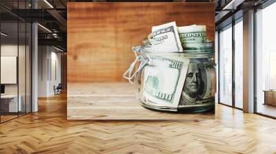 Dollar bills in glass jar on wooden background. Saving money concept. Wall mural