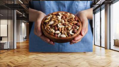 Womans hands holding a wooden bowl with mixed nuts. Healthy food and snack. Walnut, pistachios, almonds, hazelnuts and cashews. Wall mural