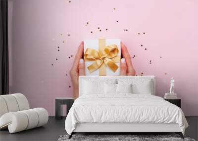 Womans hands holding gift or present box decorated confetti on pink pastel table top view. Flat lay composition for birthday or wedding. Wall mural