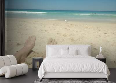 Two pairs of adult sandy feet in foreground with sandy beach and blue sea and sky background Wall mural