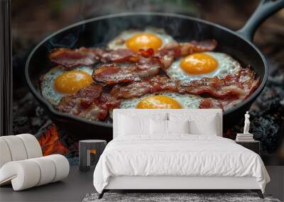 rustic camping scene with a cast iron skillet full of sizzling bacon and eggs cooking over an open fire morning light filters through misty forest creating a cozy and adventurous atmosphere Wall mural