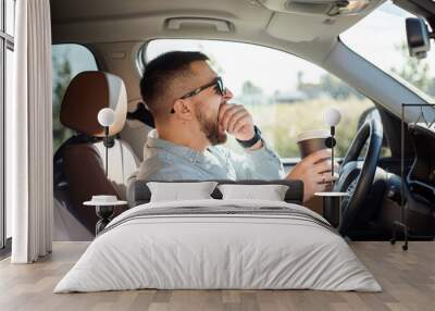 Young handsome man feeling tired and yawning while driving a car. Wall mural