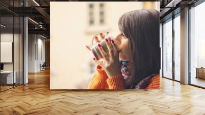 Young woman drinking coffee by the window in warm home Wall mural