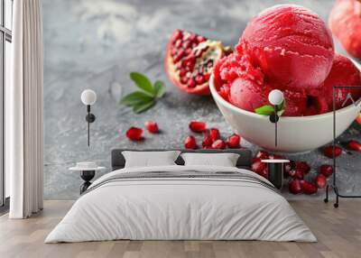 A sumptuous bowl of pomegranate sorbet is elegantly presented with fresh pomegranate seeds and leaves on a textured grey background. Wall mural