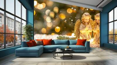 Two golden angel figurines with folded hands in prayer, surrounded by sparkling snow and warm festive lights in a peaceful winter setting. Wall mural