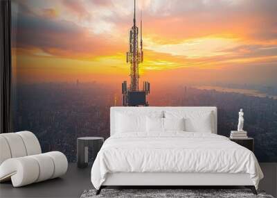 A towering communication antenna at sunset over a city skyline. Wall mural