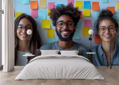 Three smiling individuals posing in front of colorful sticky notes. Wall mural