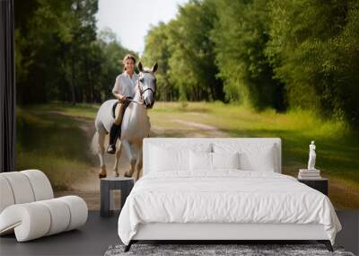 A beautiful brunette horsewoman in a white shirt rides on a horse in the forest. Wall mural