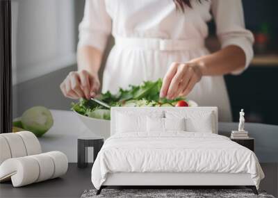 Woman in a white dress preparing fresh vegetable salad with tomatoes and cucumbers in a bright kitchen. Healthy eating concept. Wall mural