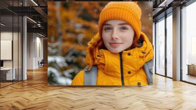 Woman wearing an orange jacket and hat, smiling in a snowy forest. Vibrant autumn background with falling snowflakes. Concept of winter outdoor activities and nature enjoyment. Wall mural