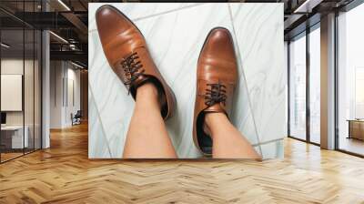 top view woman feet try to wear oversize brown men leather shoes Wall mural