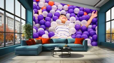 Little asian boy is playing in ball pit playground with purple and white ball Wall mural