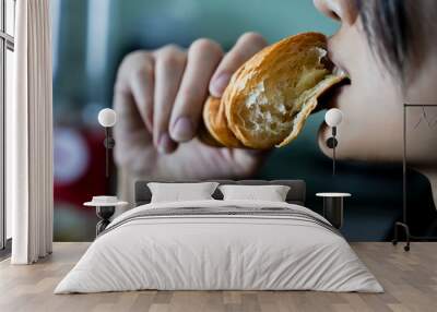 Woman eating a croissant in her hand, closed up shot. Wall mural