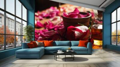 Clay bowl and aroma oil glass bottle among roses petals on the wooden table, natural raw material, selected focus Wall mural