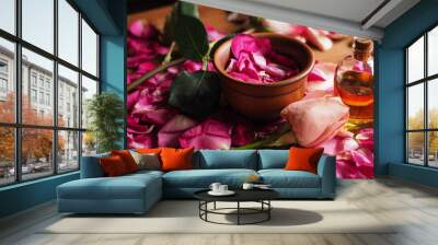 Clay bowl and aroma oil glass bottle among roses petals on the wooden table, natural raw material, selected focus Wall mural