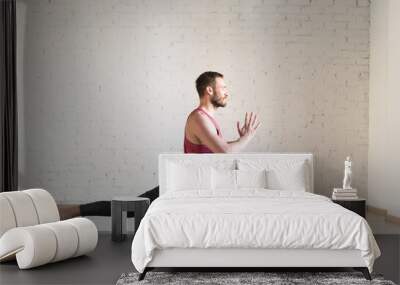 Warrior pose. Caucasian fit man stands in deep stretching and doing yoga in fitness studio, side view, selective focus. Wall mural