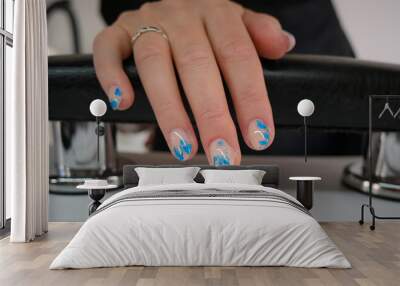 Woman hand with fresh gel polish and blue nail art design, resting on a black leather armchair in a beauty salon Wall mural