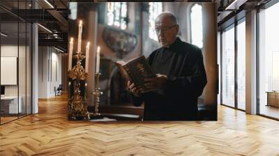 Senior priest holds a Bible and looks at the camera while standing in the church. Concepts about religion, belief, god Wall mural