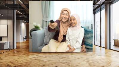 Smiling muslim mother and daughter watching television Wall mural