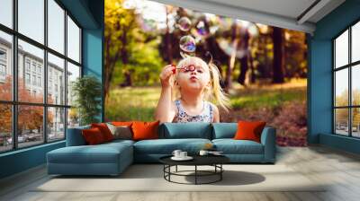 Funny little girl blowing soap bubbles in summer Wall mural