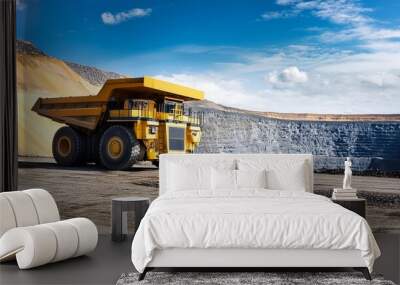 A heavy-duty dump truck operating in a mining site, showcasing industrial machinery against a backdrop of blue skies and mountains. Wall mural