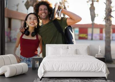 Beautiful couple having fun outdoors. Portrait of an excited young couple with skateboard. Wall mural