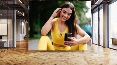 Beautiful woman resting from working out. Young athlete woman sitting on the bench and using the phone after training.	
 Wall mural