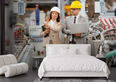 Businessman and businesswoman in factory. Man and woman in suits with helmets in factory discussing work. Wall mural