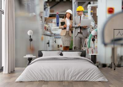 Businessman and businesswoman in factory. Man and woman in suits with helmets in factory discussing work. Wall mural