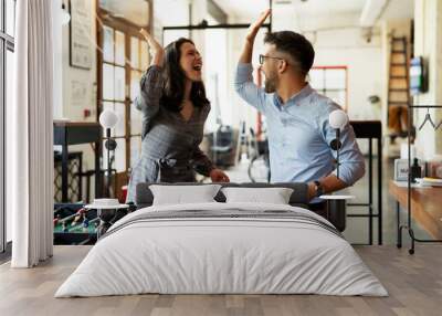 Colleagues having fun at work. Businessman and businesswoman playing table soccer. Wall mural