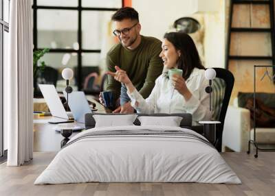 Colleagues laughing in office. Businesswoman and businessman drinking coffee. Wall mural